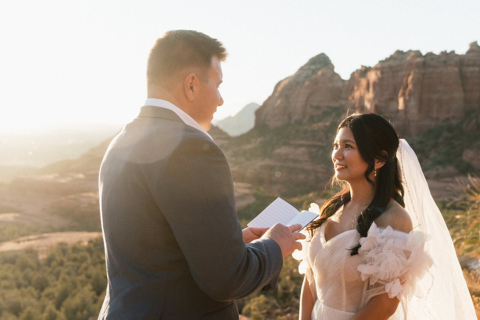 Groom reading vows to the bride during their emotional Sedona elopement ceremony at Merry Go Round Rock, with golden light and red rock cliffs in the background.