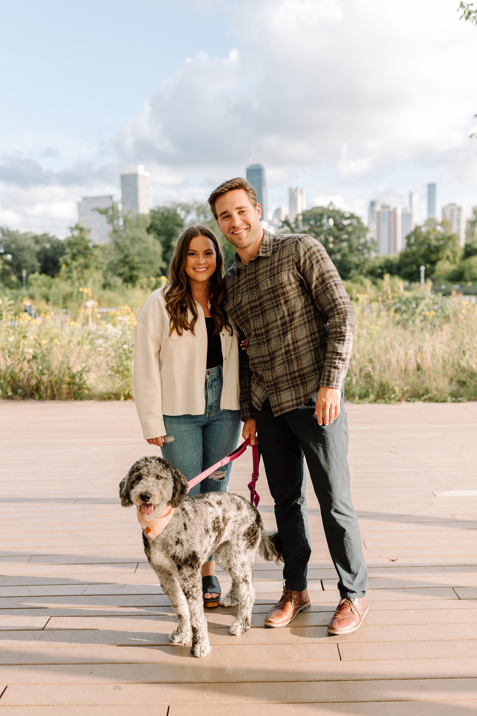 Newly engaged couple posing with their dog in front of the Downtown Chicago Skyline