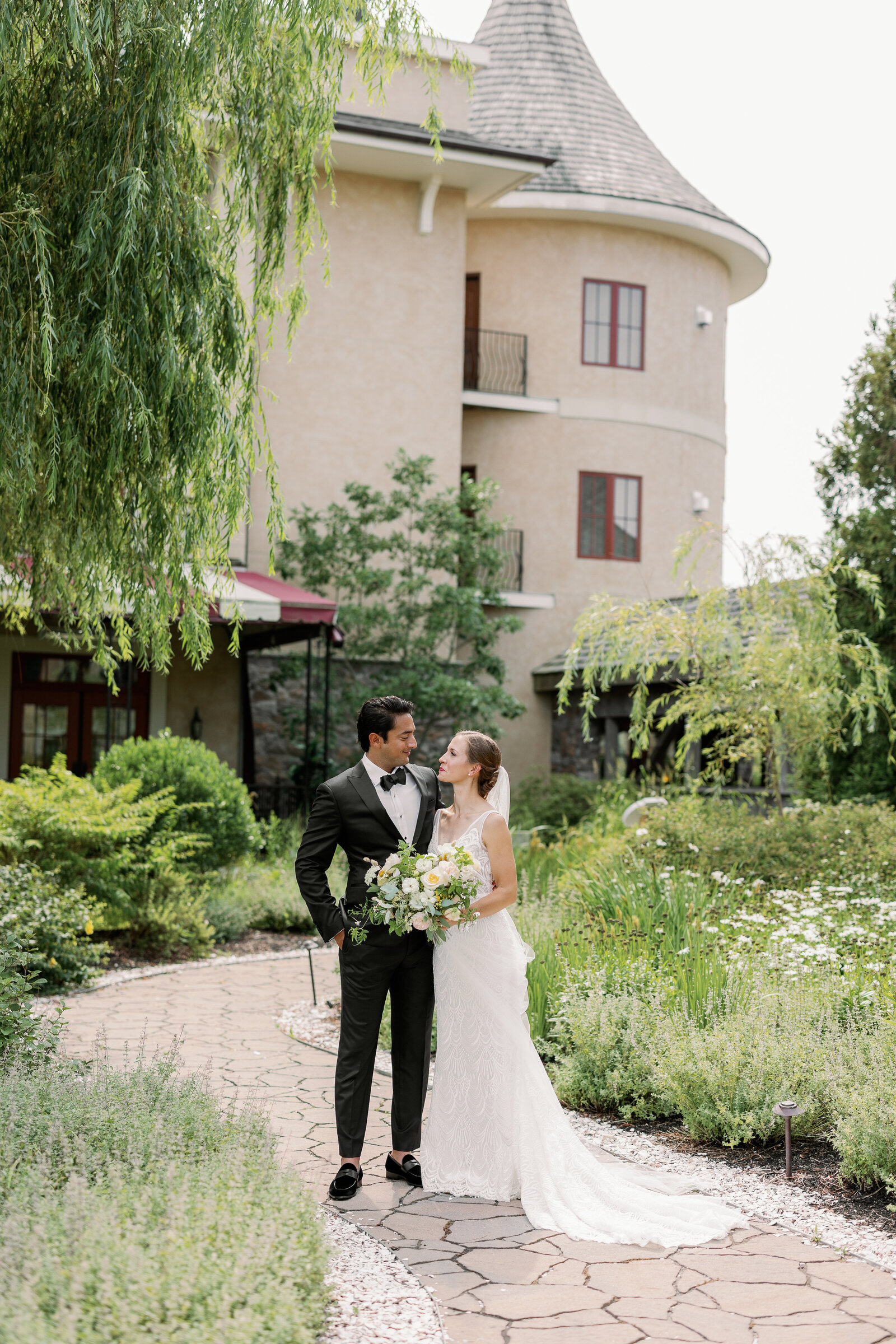 Wedding couple standing on a small path in front of a large, cottage like building.