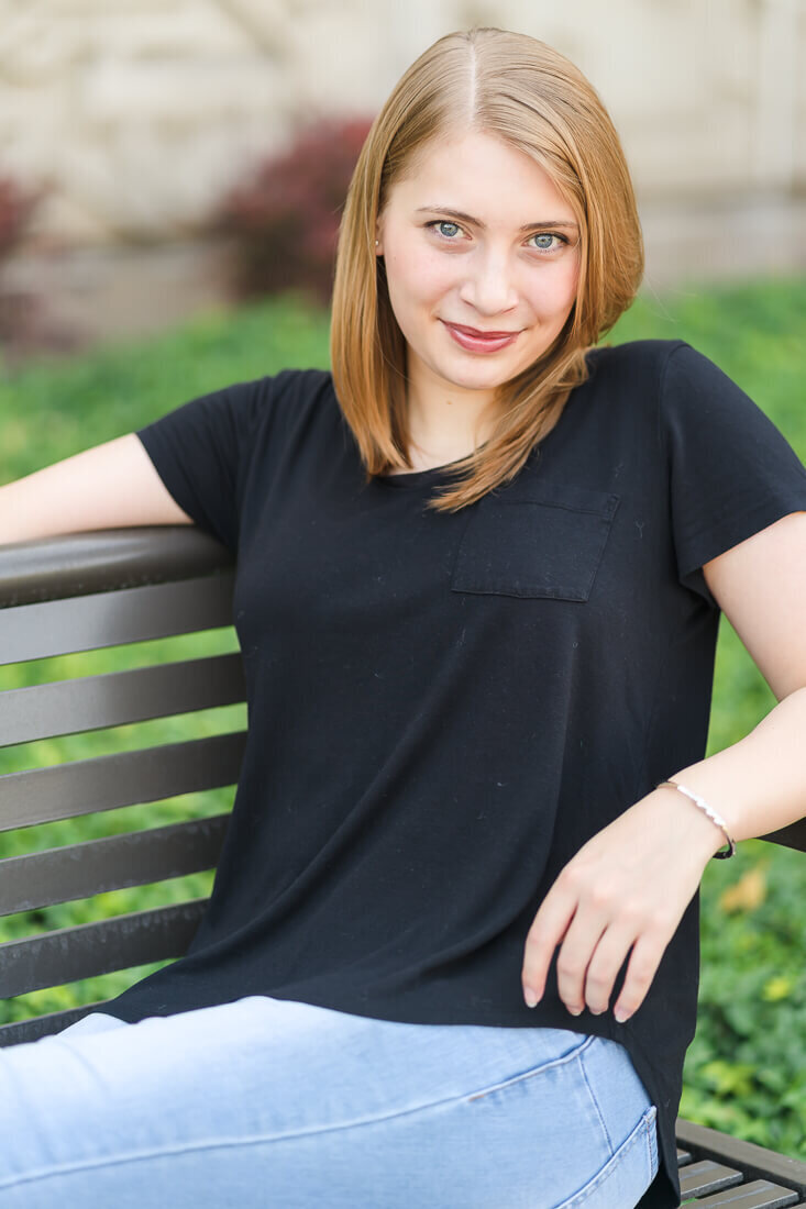 Close-up of a high school senior girl wearing a black t-shirt and light blue jeans sits with her feet up on a bench at BYU in Provo