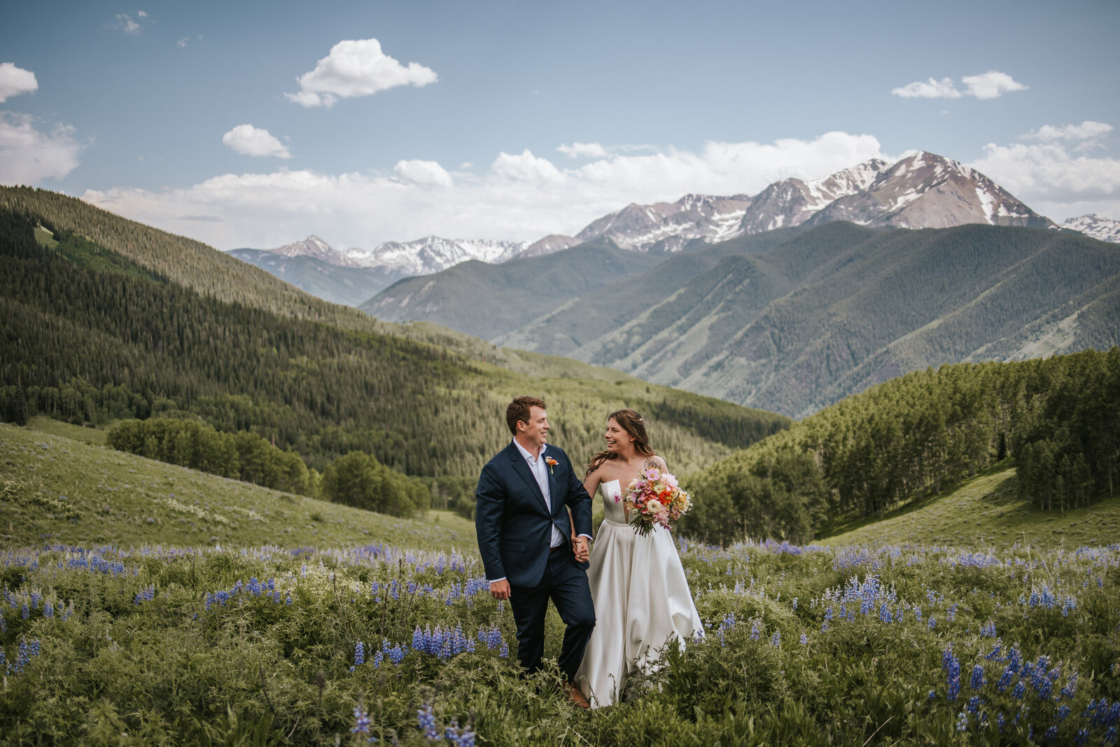 Couple smiling at each other and walking in the wildflowers in the mountains on their elopement wedding day.