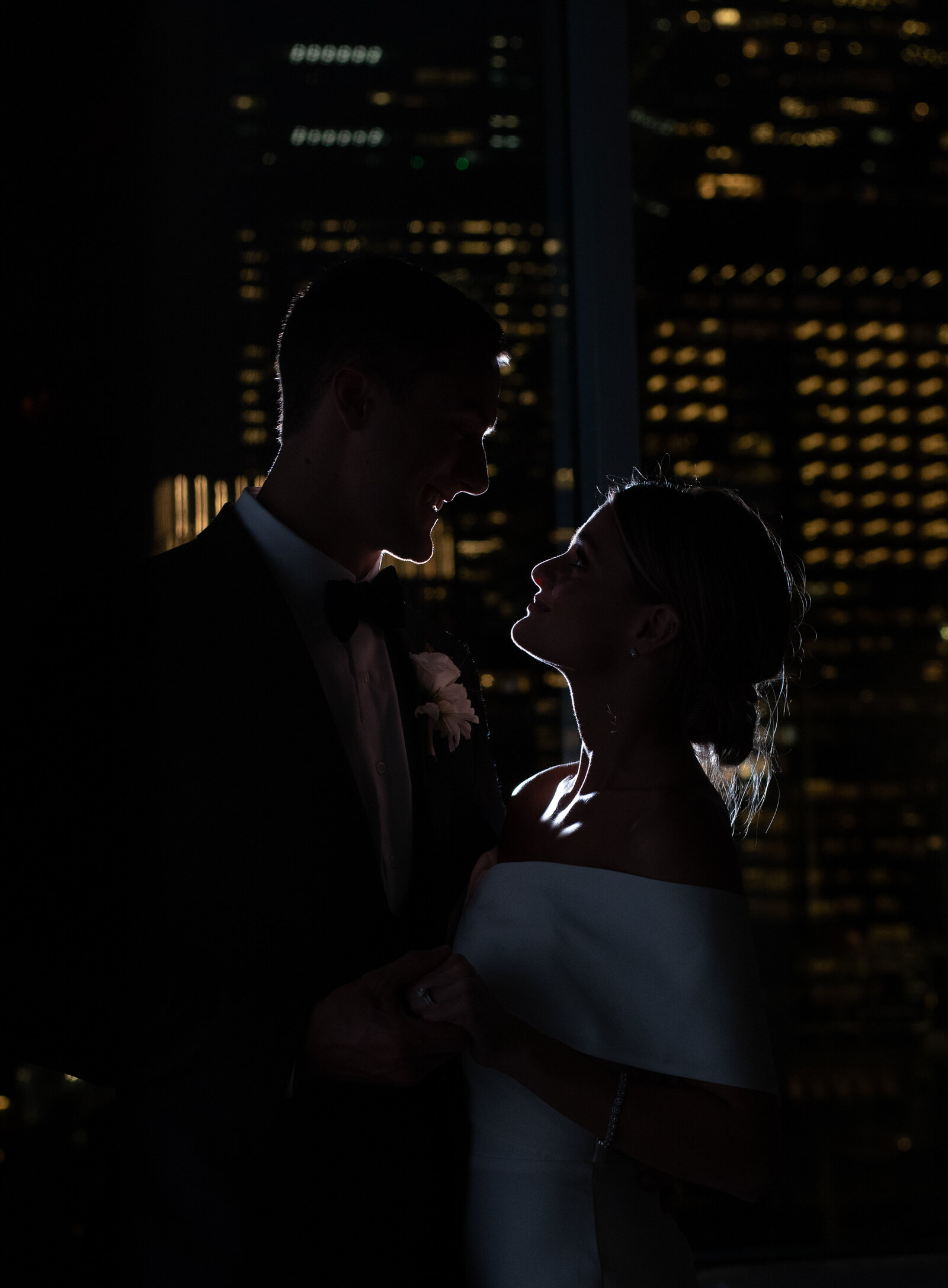 black and white picturere of the outline of a couple being backlit.  They are in the Glasshouse in  Ghelsea with the city lights lit behing them.