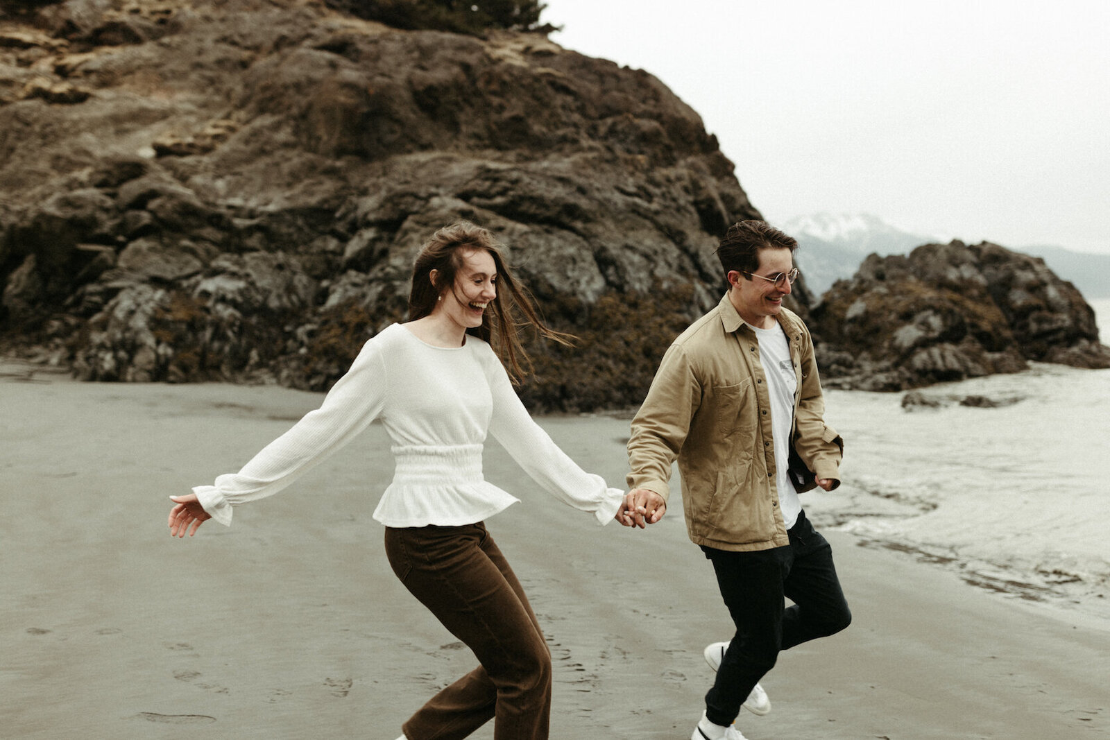 couple holding hands and running along the beach