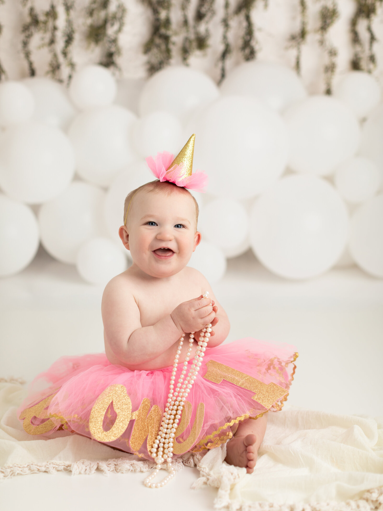 one year old girl in pink tutu holding pearls for first birthday photoshoot