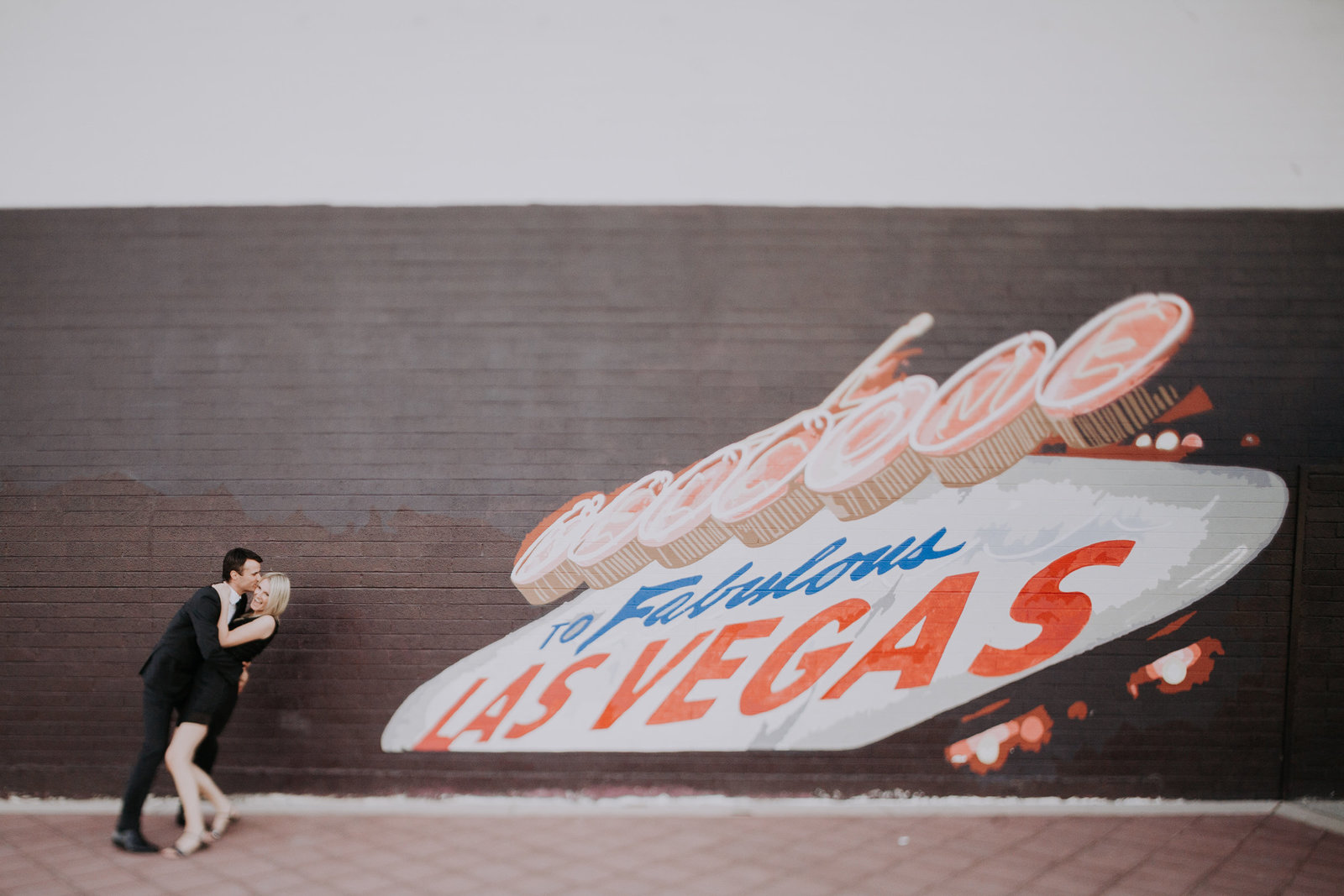 couple laughs together in front of mural of welcome to las vegas sign