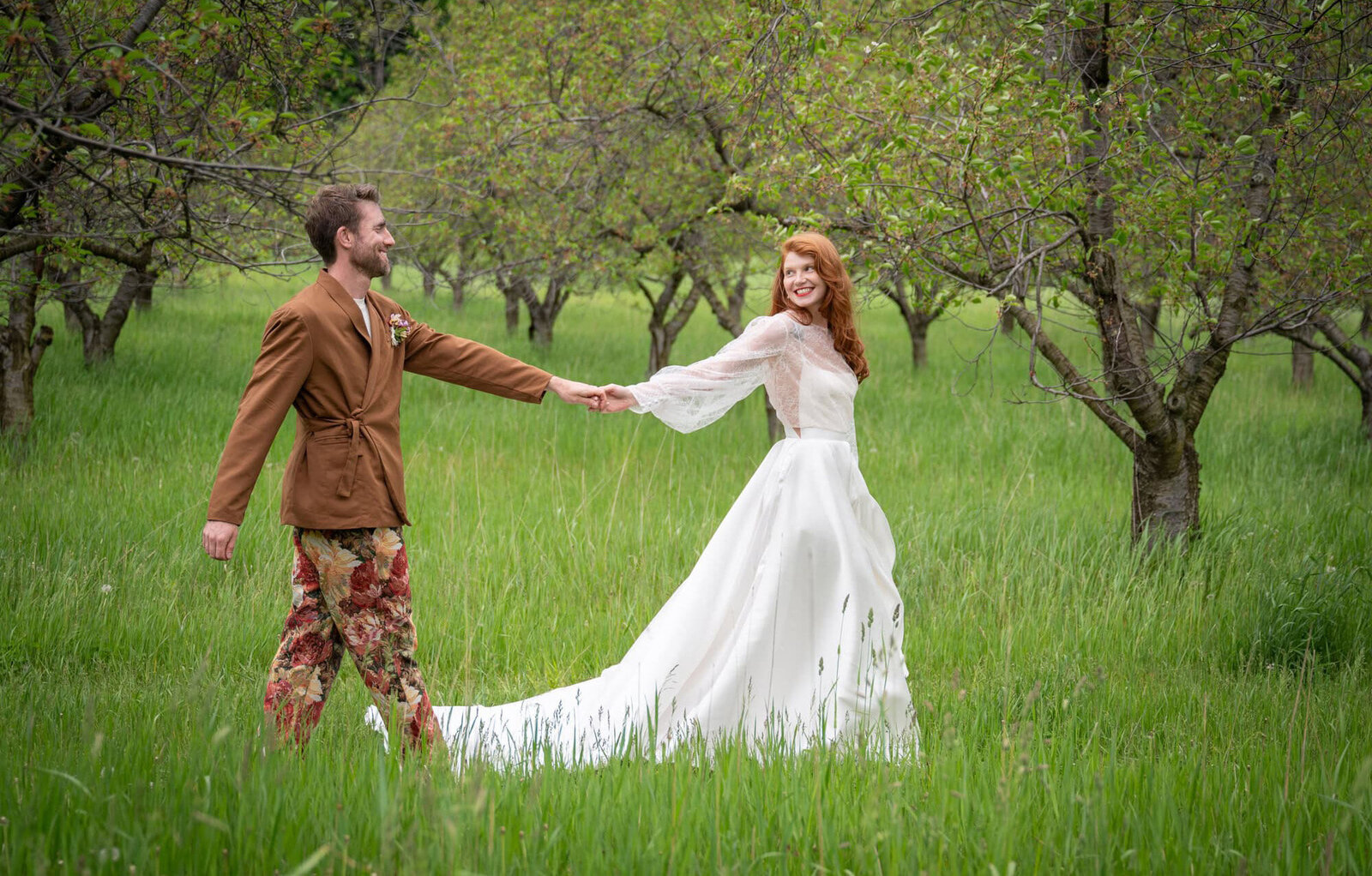 bride leads groom through apple orchard