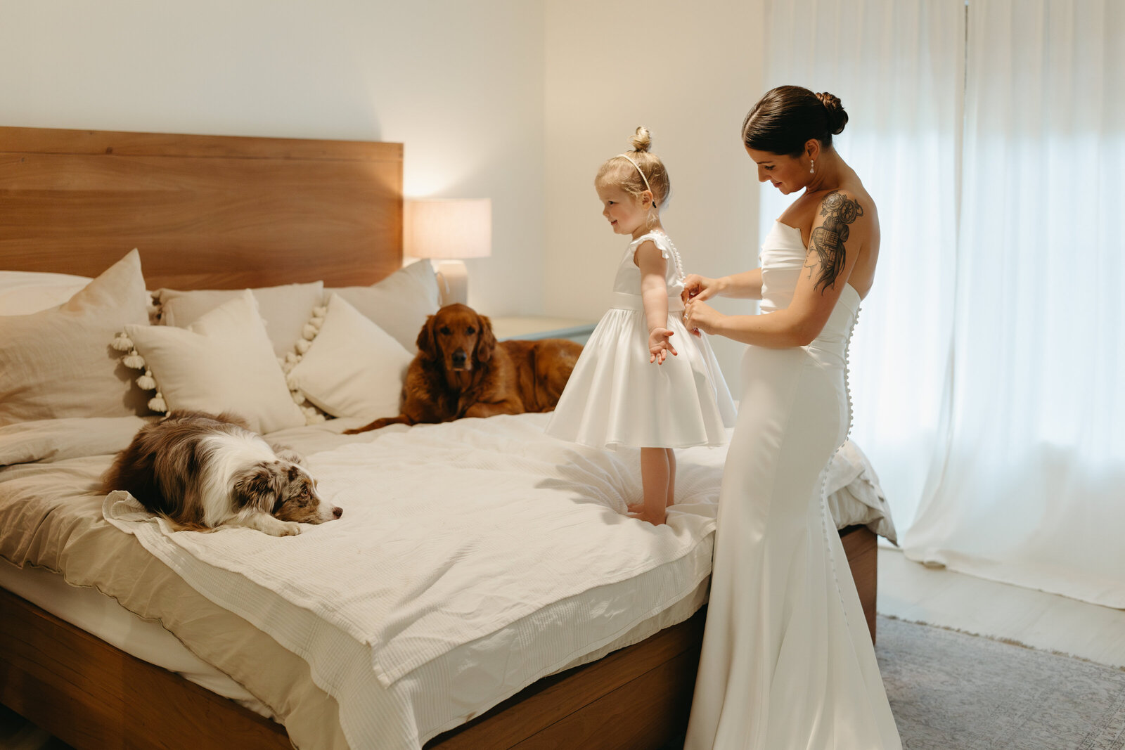 A bride helps her young daughter get dressed into her wedding attire. 