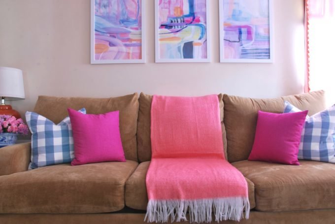 A tan sofa with color throw pillows and three framed art pieces.