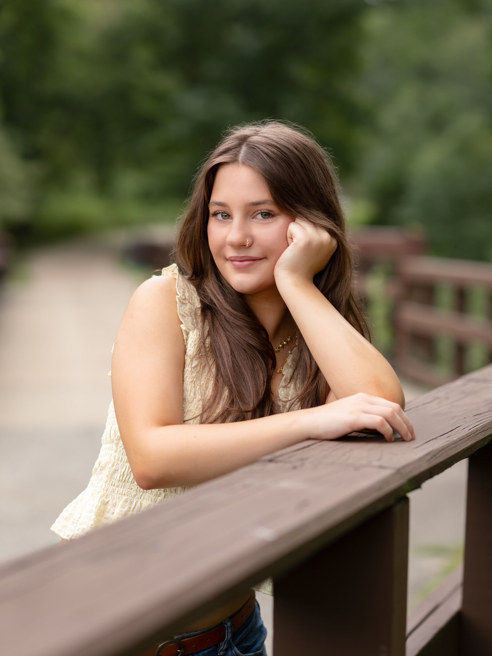 senior girl in yellow shirt leaning on fence for senior portraits