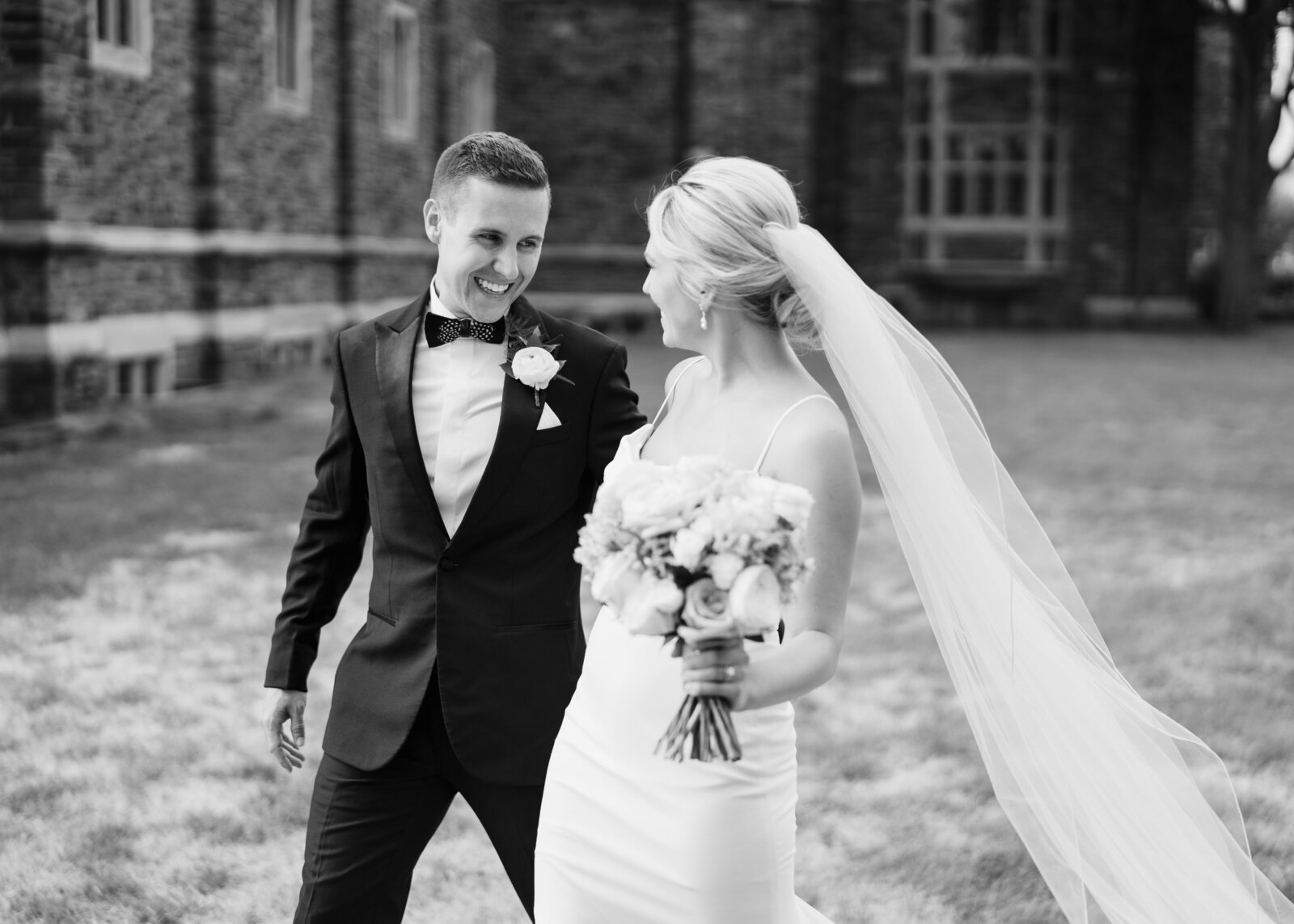 Bride and groom smile at each other as they walk on the lawn of the First Congregational Church in Columbus