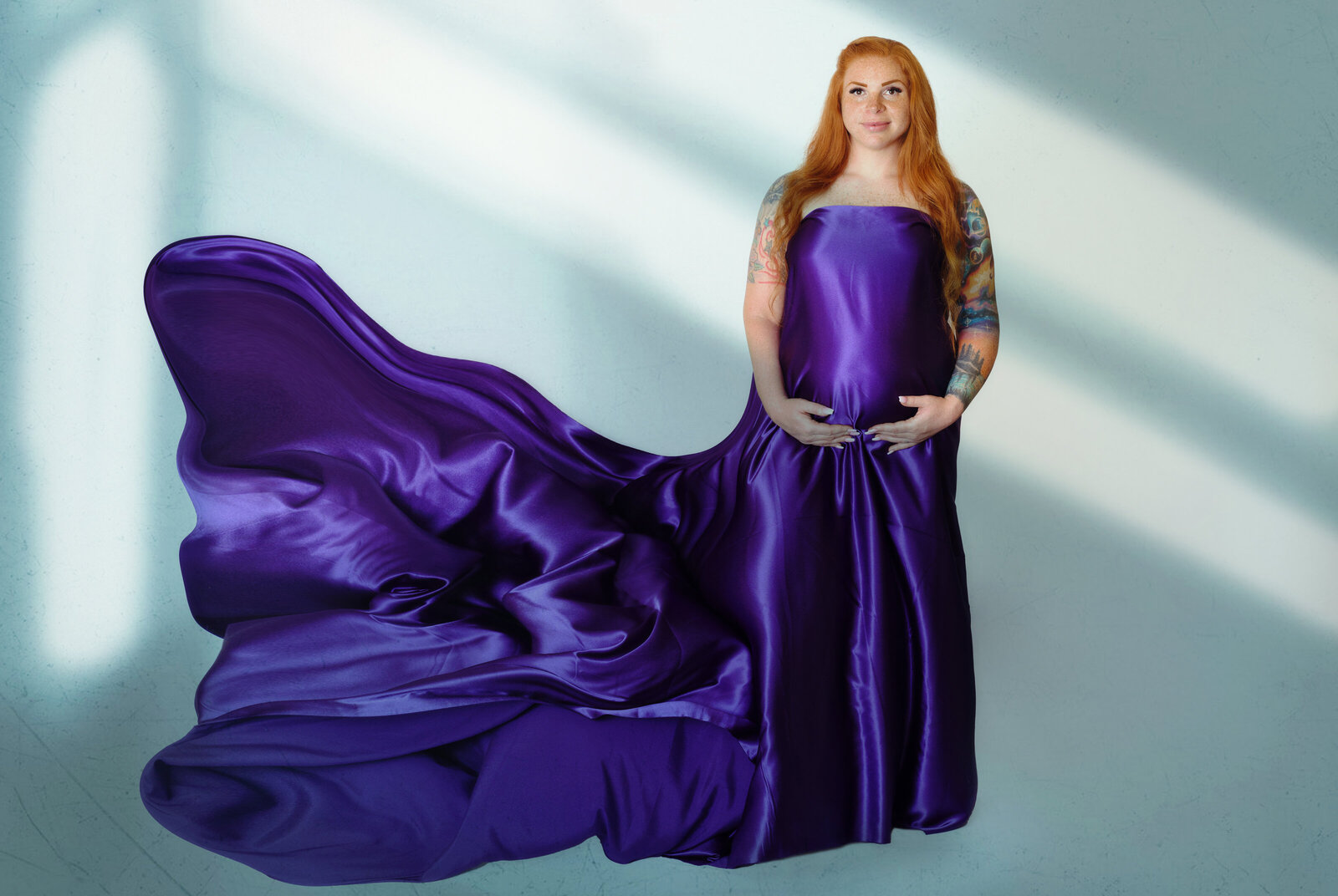 Maternity Photographer, A woman wears a pregnancy gown in a studio, sun rays shine on her