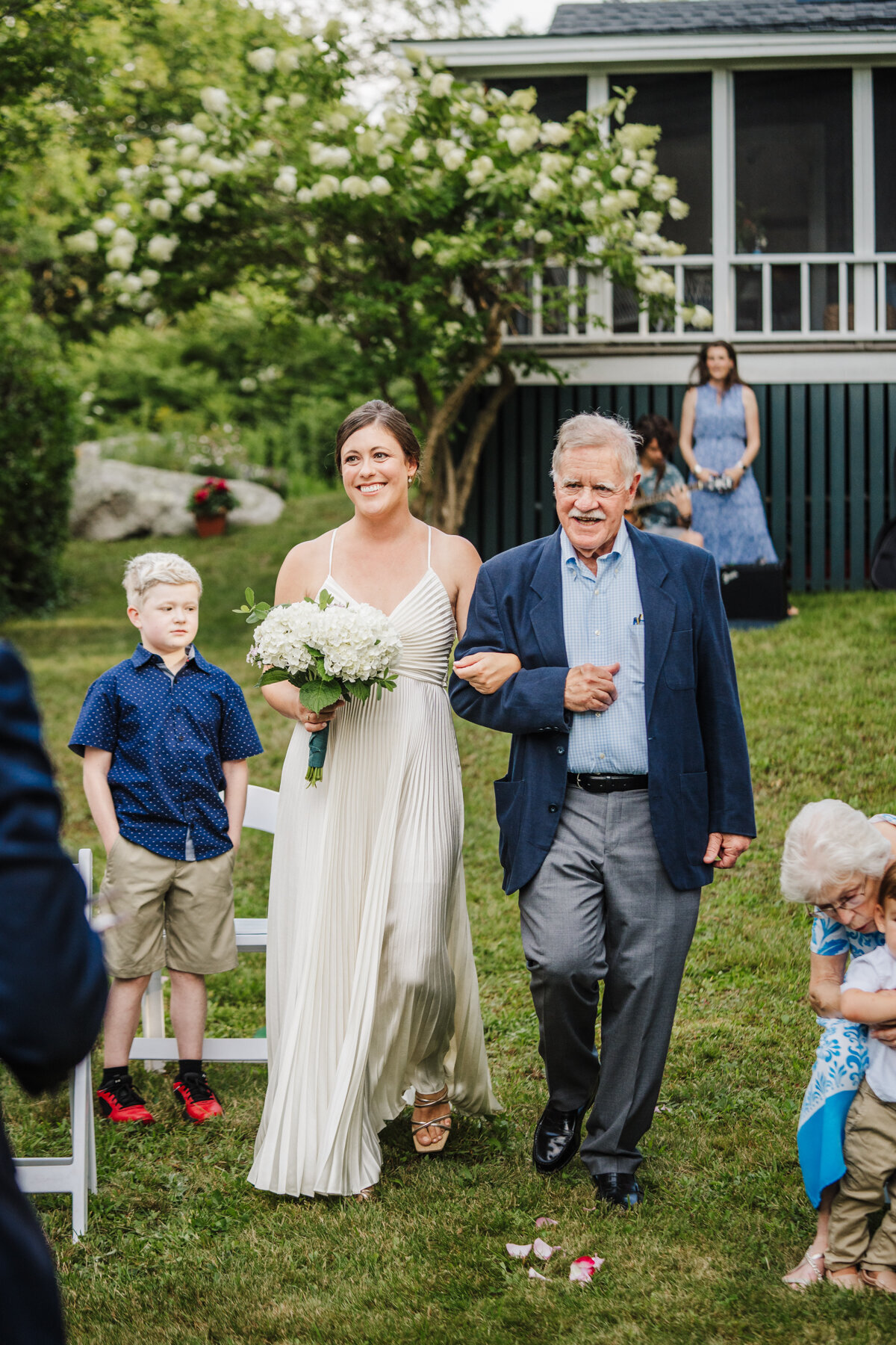 father walks his daughter down the aisle on her wedding day in cottage backyard