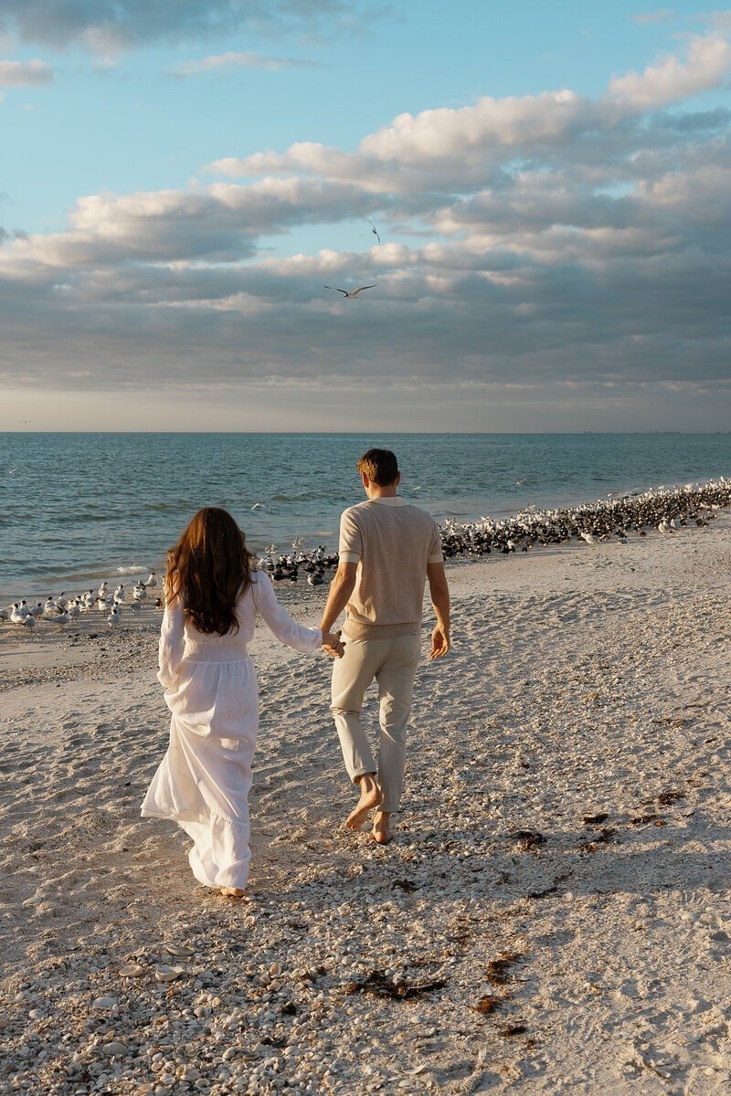 couple holding hands and walking on beach by proposal photographer naples fl