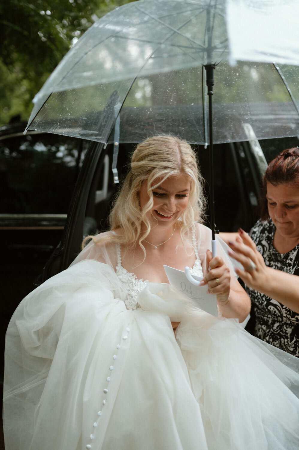 Bride just got out of her wedding car with her assistant holding umbrella for her