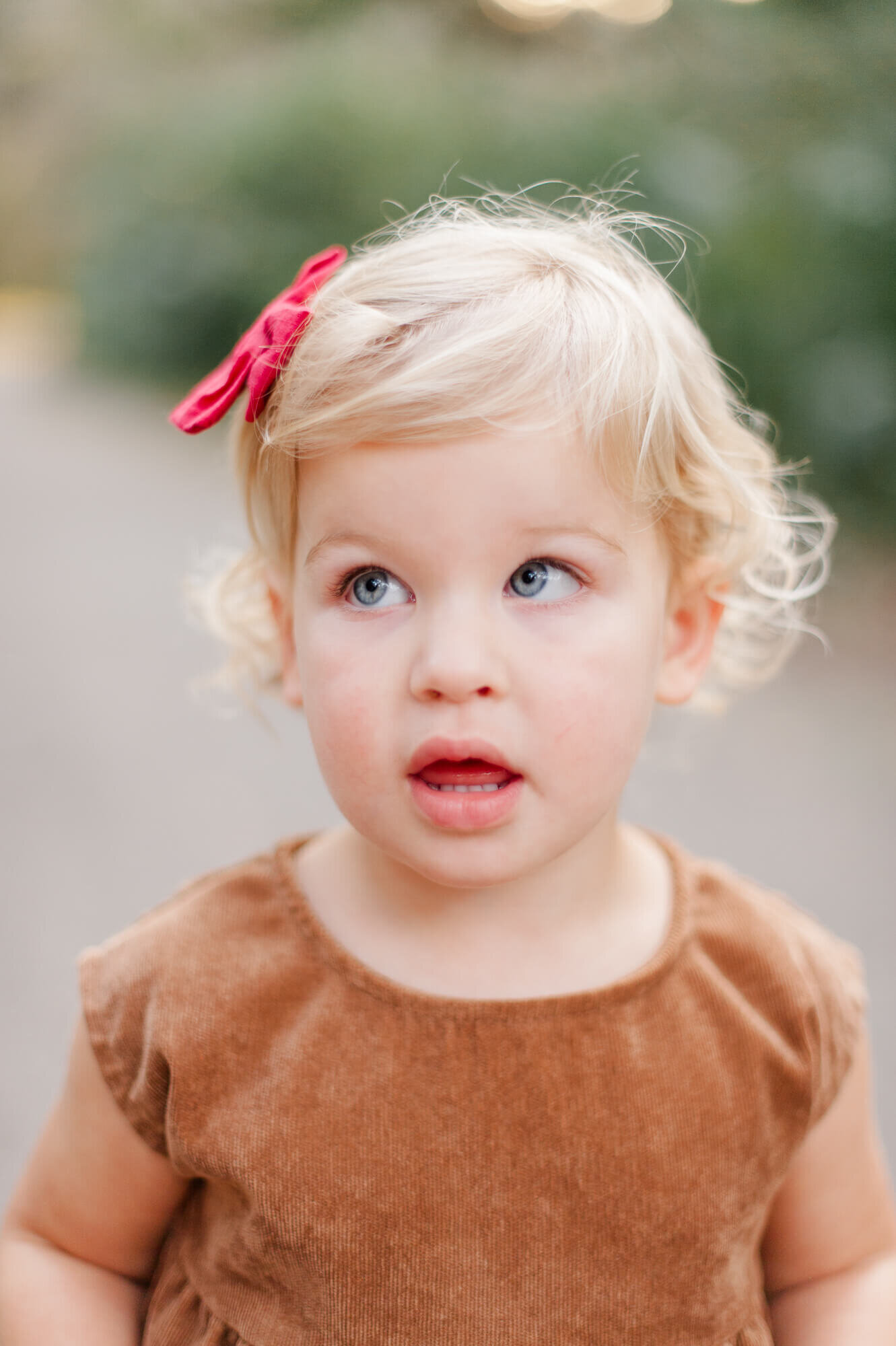 Sweet blonde curly headed toddler smiling and looking away from the camera