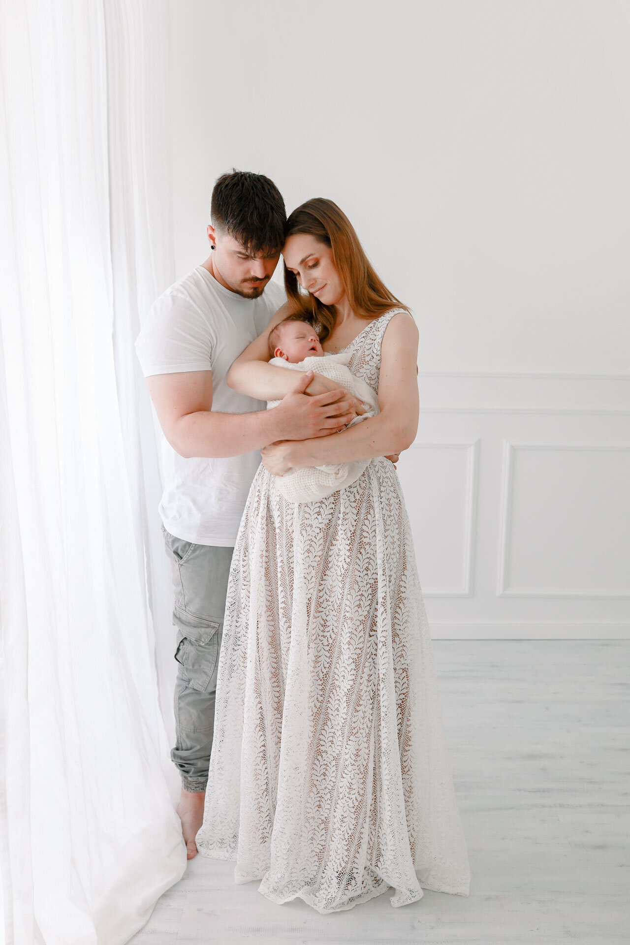 Familienfotografie in Bielefeld von Mama in langem weißen Kleid und Papa die ihr Neugeborenes im Arm halten.