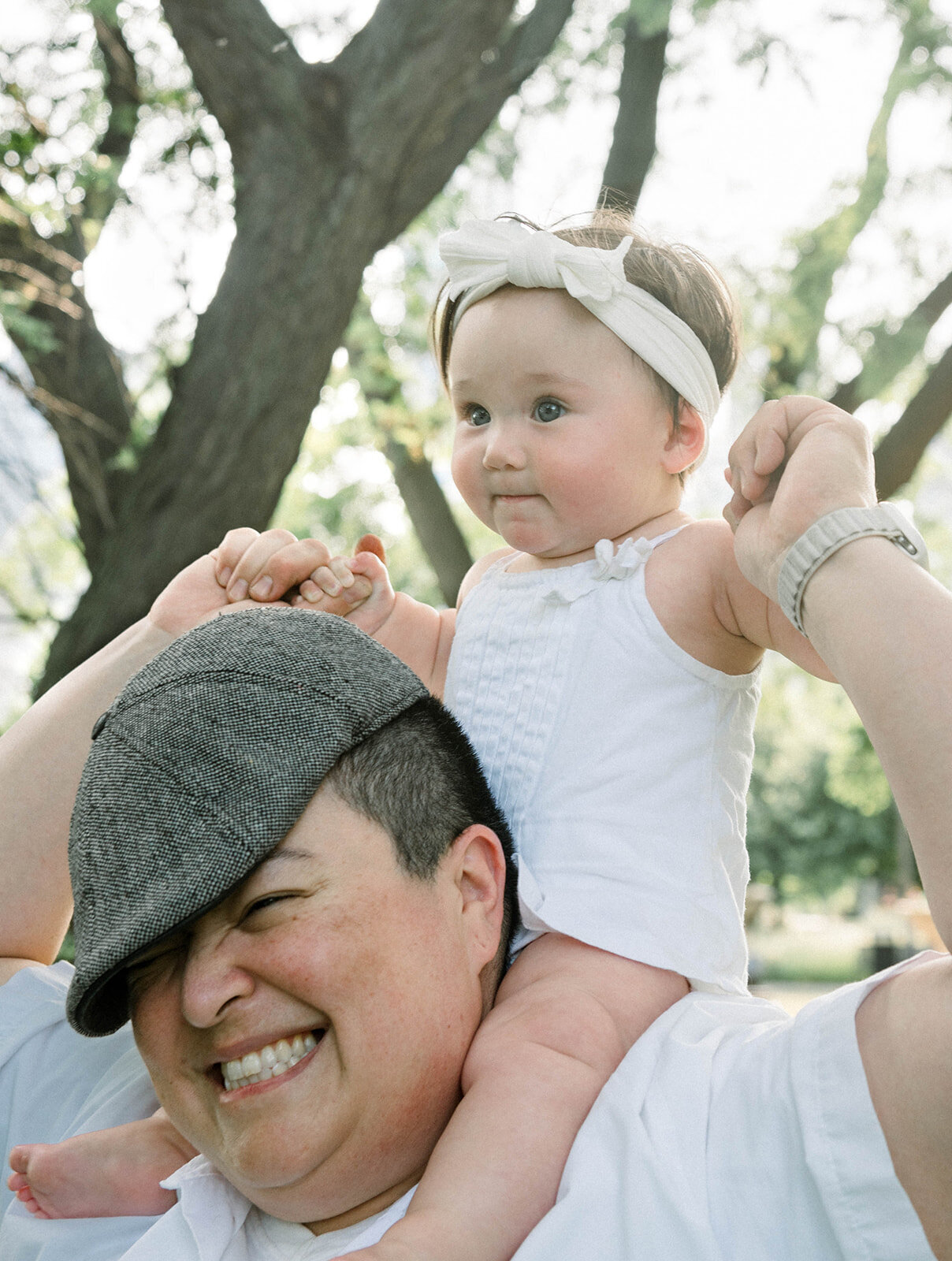 A baby on top of her parent's shoulders outside in a Chicago park
