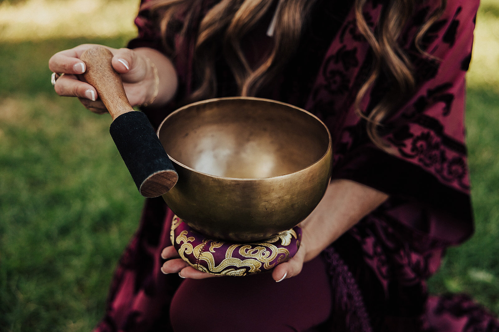 Patty in a maroon dress with her gold sound bowl 