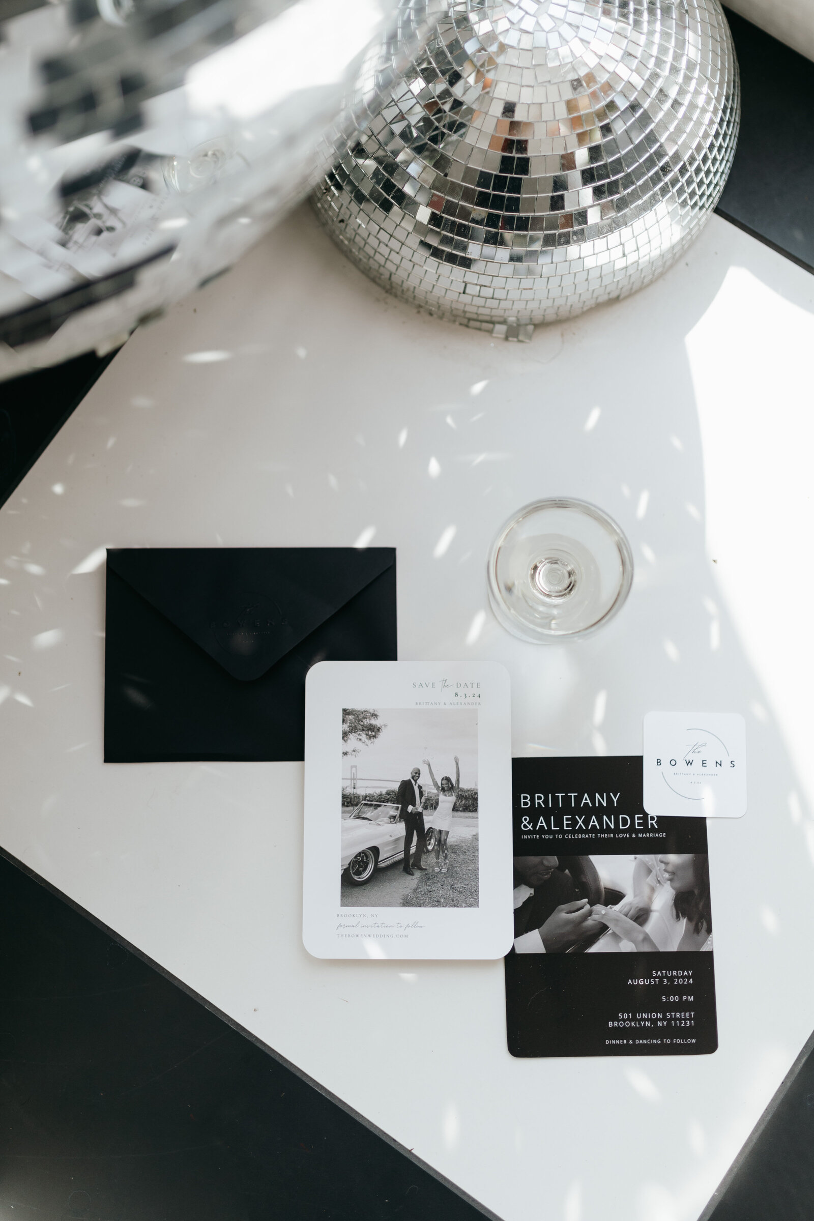 Wedding invitation flat lay with martini glass and disco ball on white square surrounded by a black backdrop | Emma LeeAnn Photography