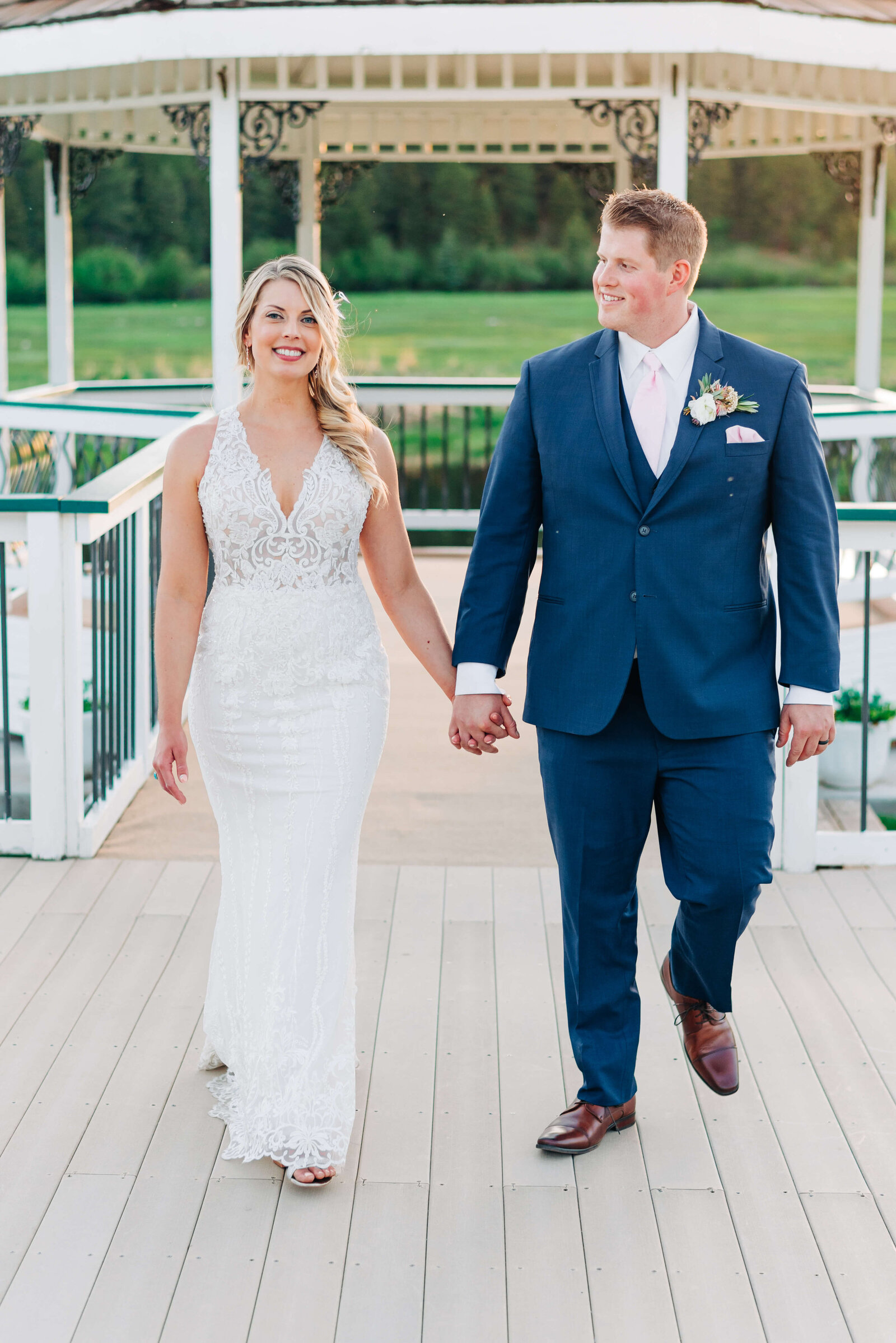 Virginia wedding photographer takes an image of a newly married couple walking together on a white bridge and smiling at the camera