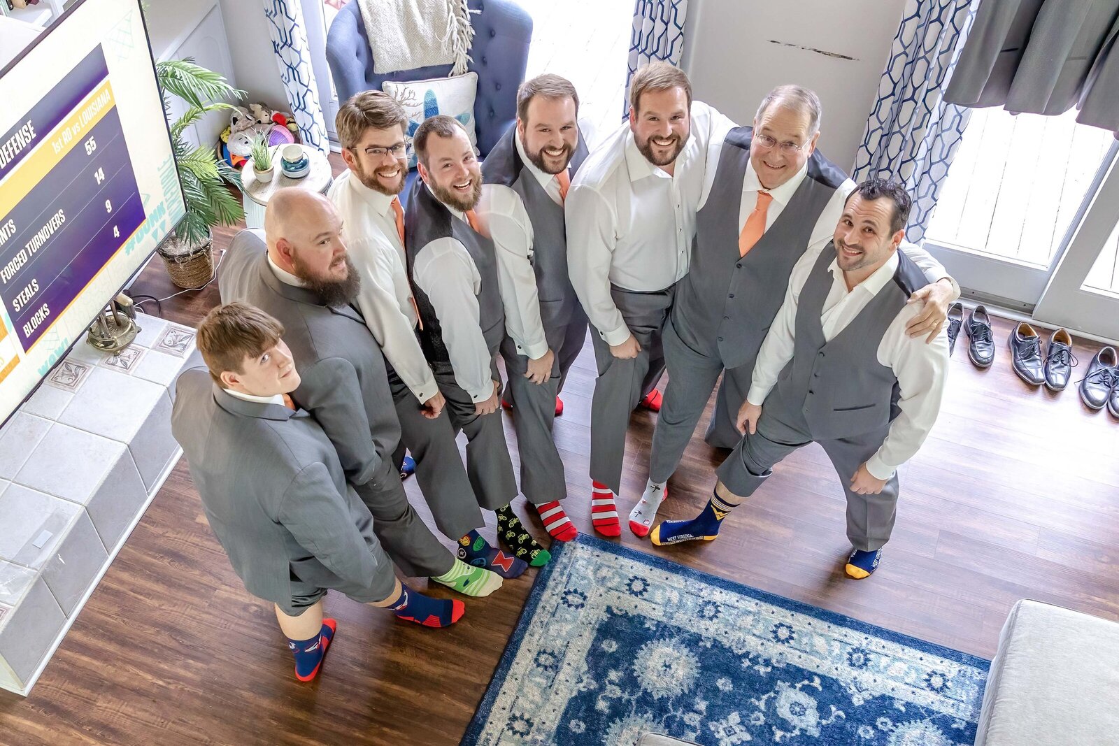 The groom and groomsmen pose in mismatched fun socks while getting ready indoors, captured during a Wilmington, NC wedding, blending humor and authentic wedding day preparations.