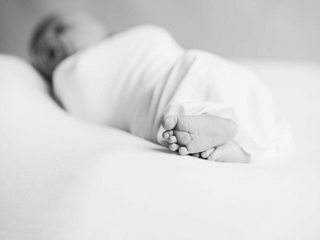 black and white photograph of newborn baby wrapped in a white swaddle, close up of feet