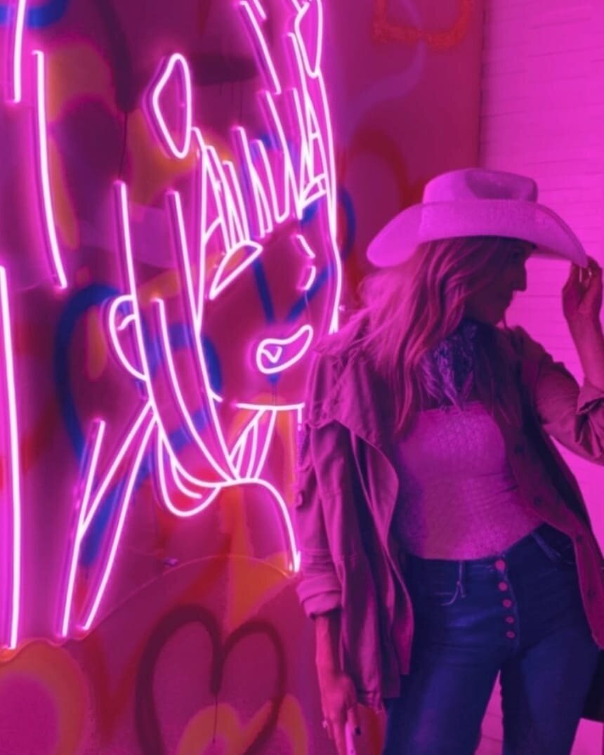 Woman having fun in cowboy hat next to neon sign