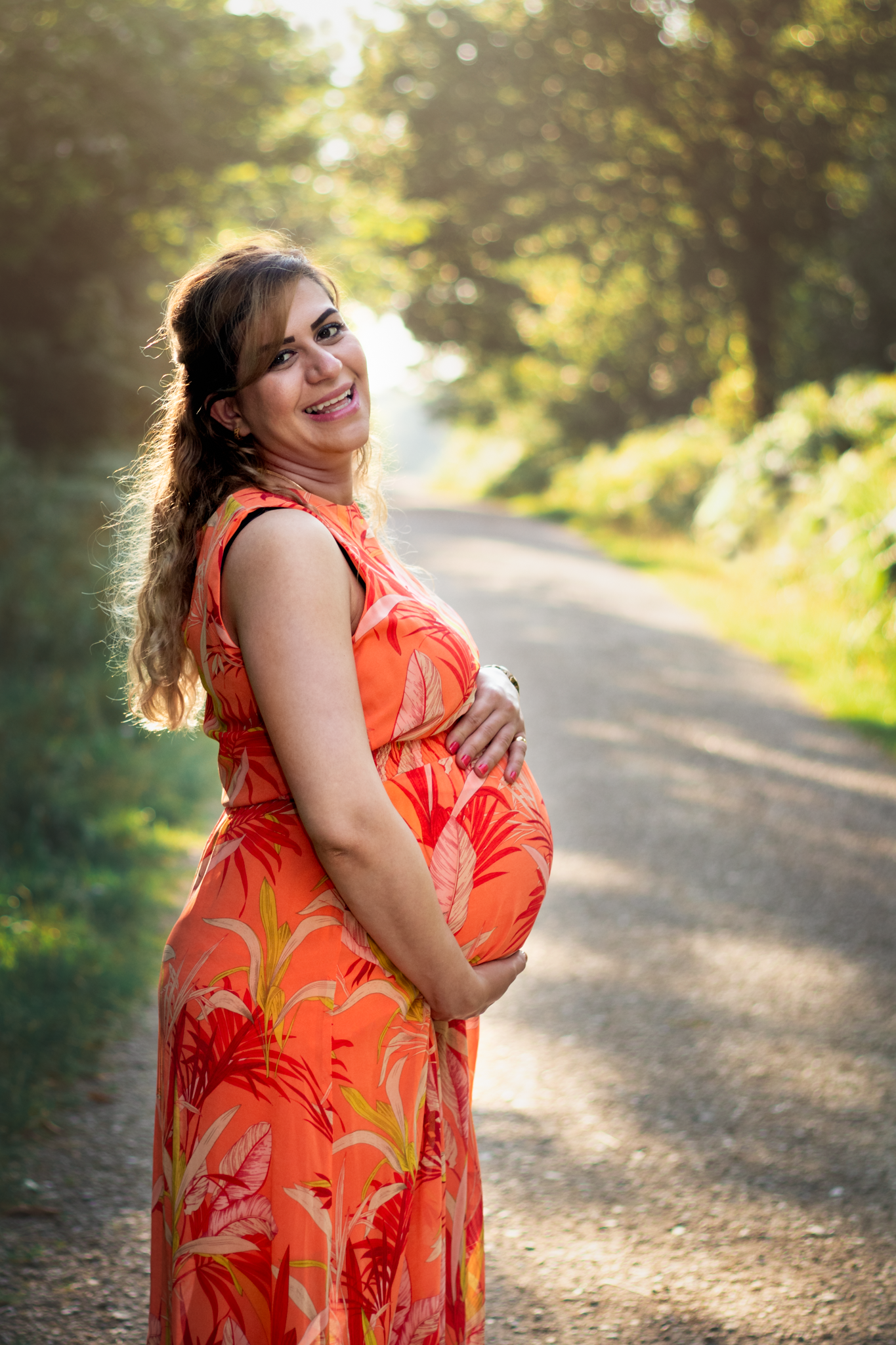 Woman holds her baby bump whilst stood on sunny path for photo