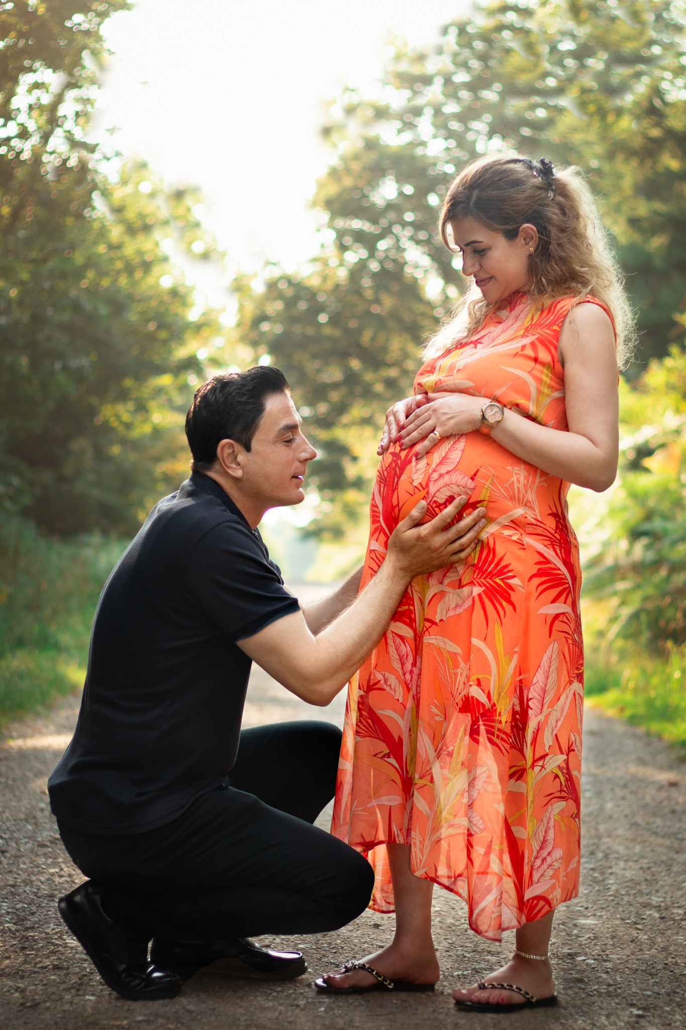 Husband kneels to hold his wife's baby bump  during photography session