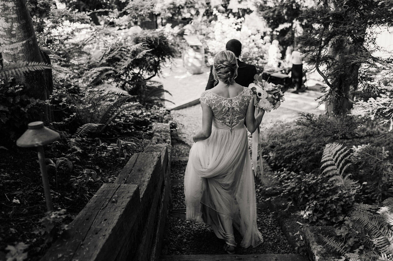 A stunning black and white image of a bride wearing a flowy wedding gown walking down a wooded path