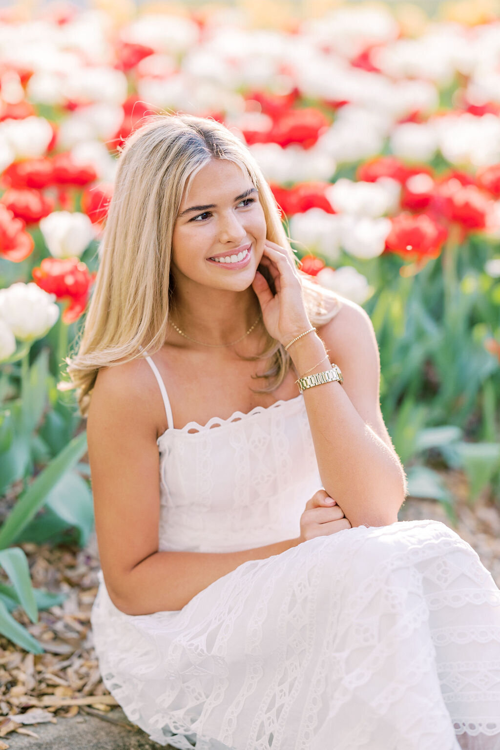 Girl in white dress smiles with red flowers in background