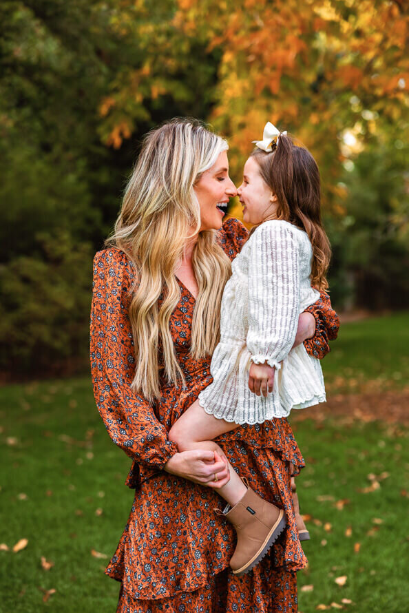Mom rubs noses with her young daughter with the fall leaves behind her at Writers Vista Park during their family photos with Angela Marie Media.