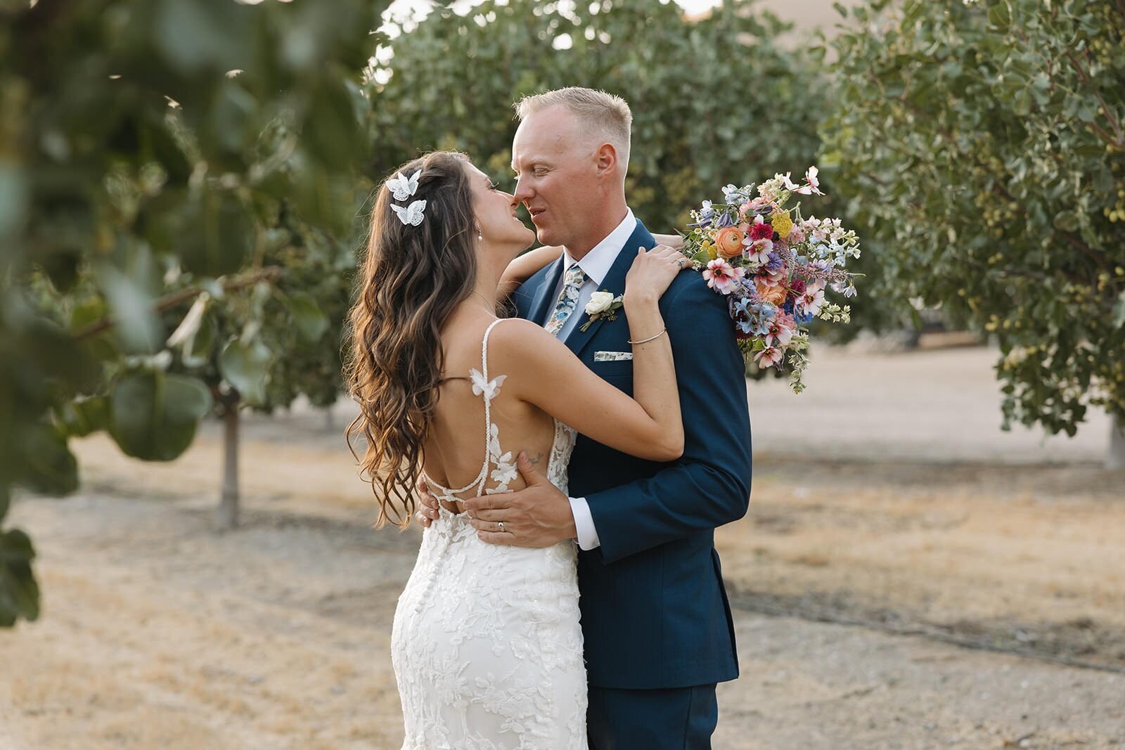 Nicolette and Alex embracing in a pistachio orchard on their wedding day in San Miguel, California