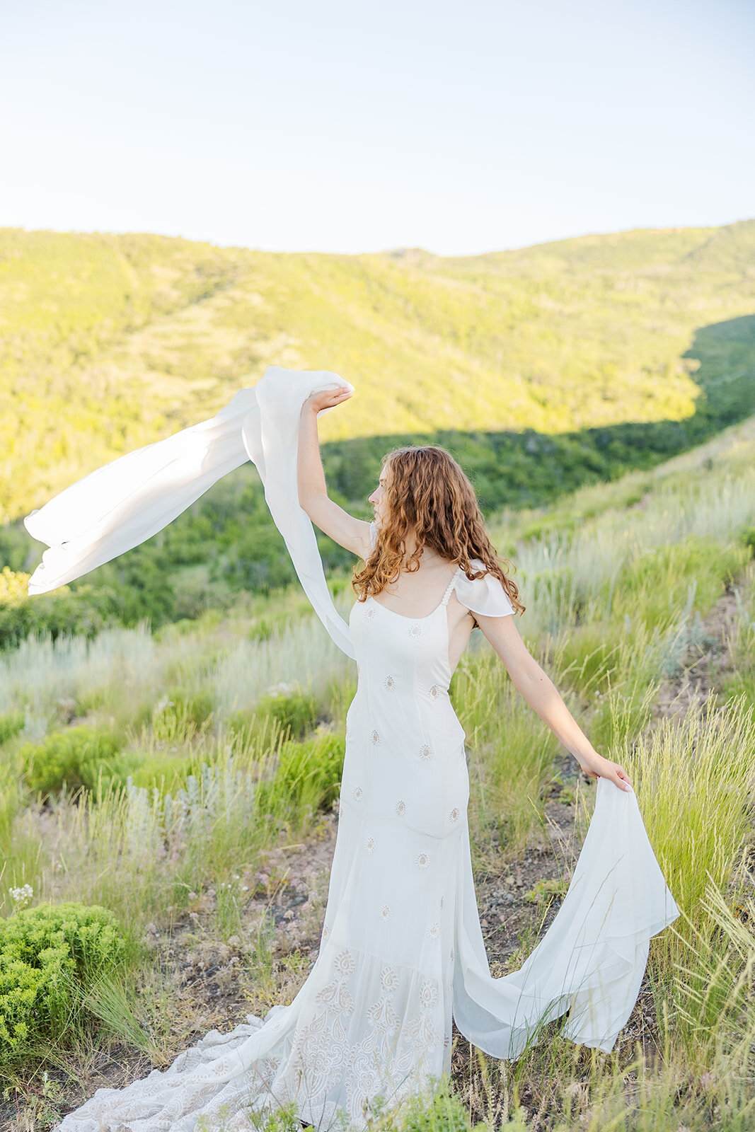 Bride playfully posing with her flowing dress during her elopement, set against a stunning mountain backdrop, capturing the essence of love and adventure in a picturesque outdoor setting