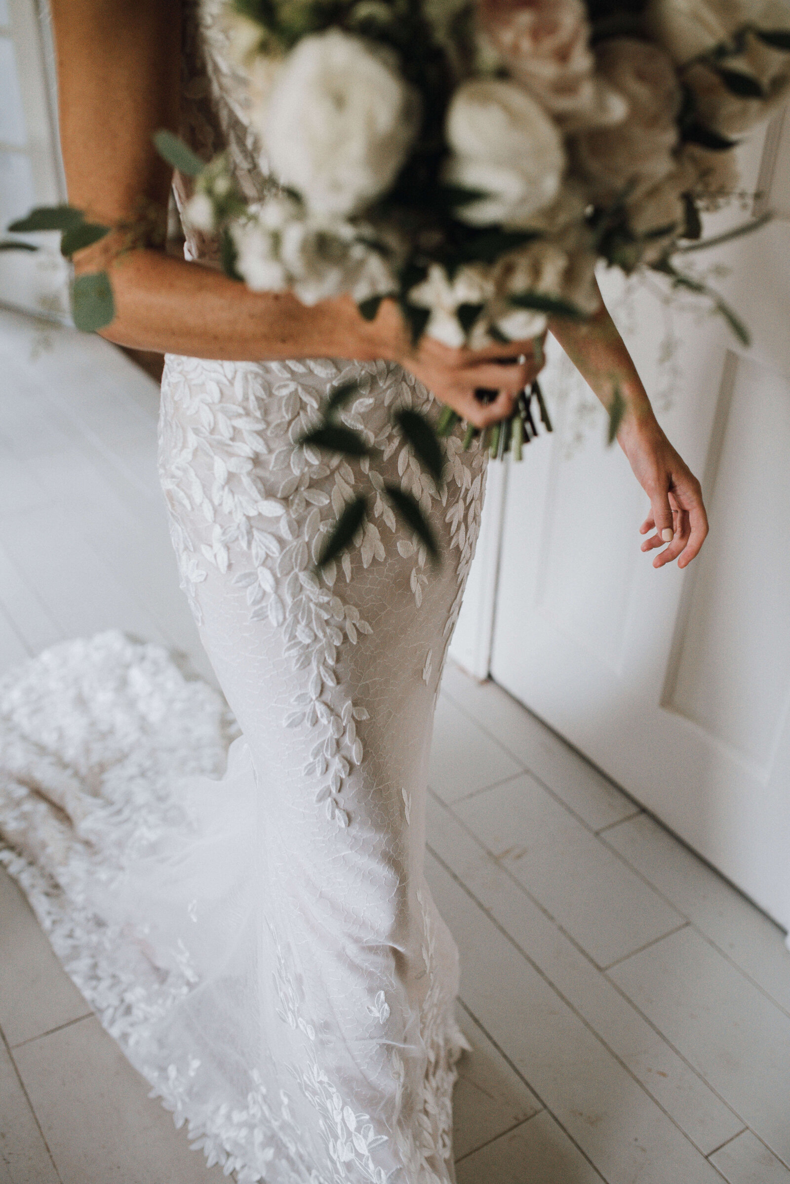Detail of a bride in a lace gown with a train carrying a white and blush bouquet