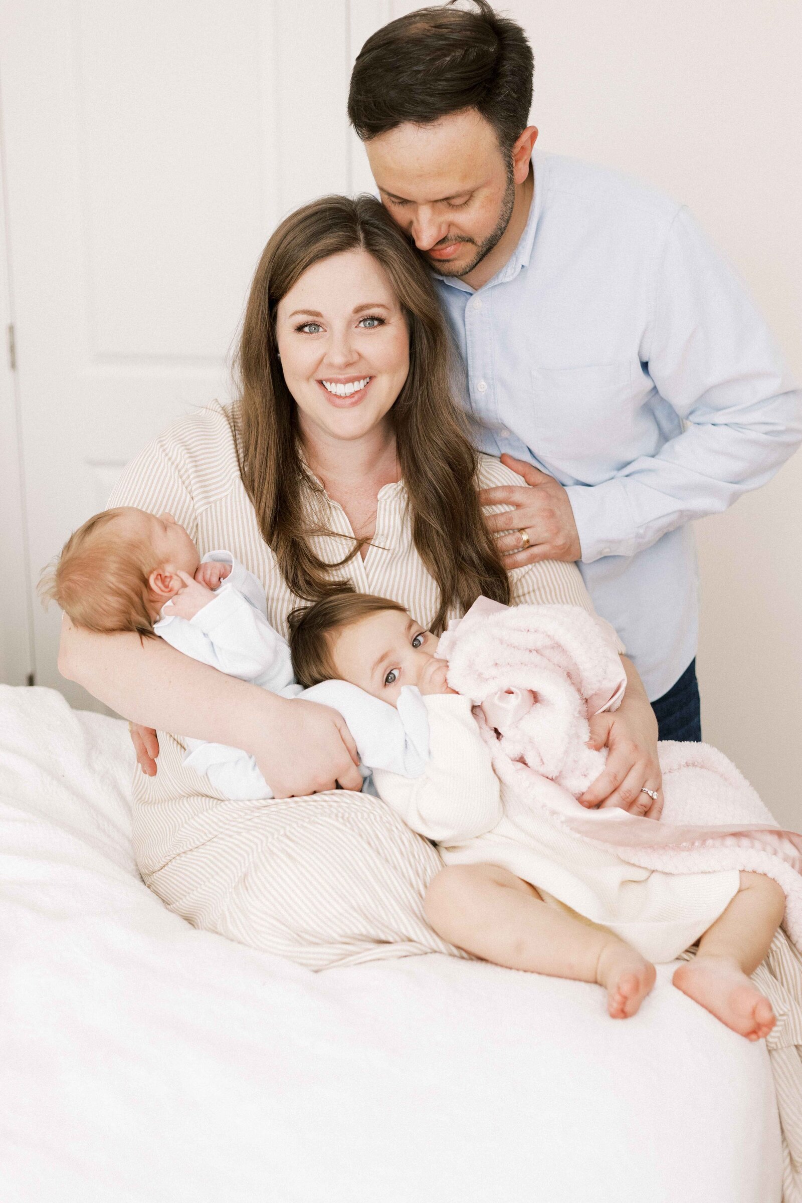 mom holding children sitting on the bed during newborn photos in peoria illinois 