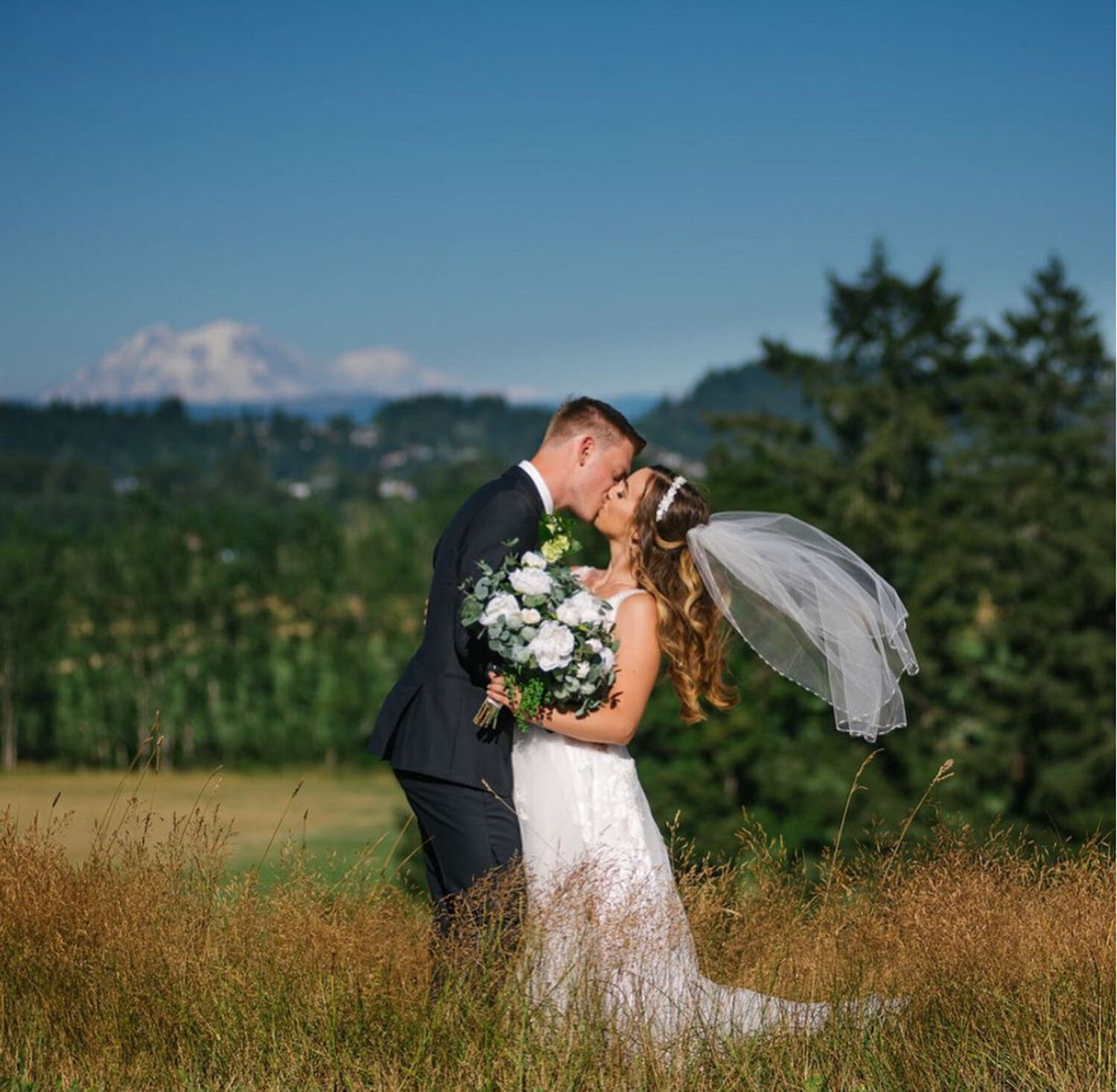 A bride and groom sharing a kiss in a picturesque meadow with a mountain in the background
