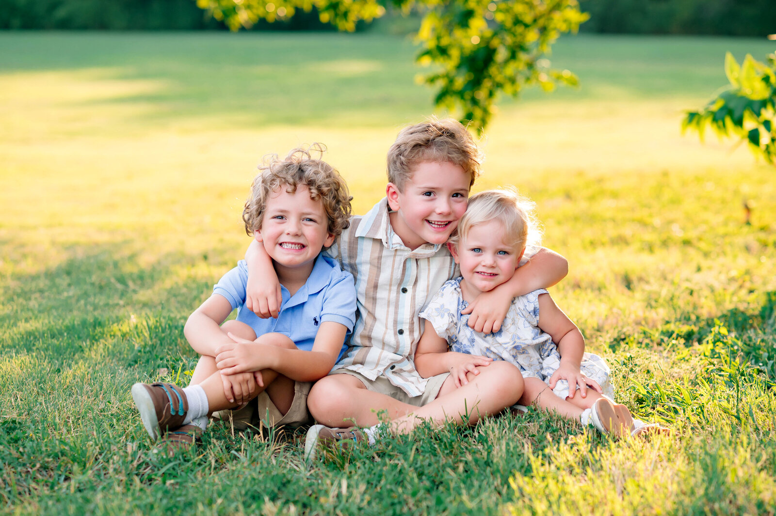 Three siblings laughing together in a field during a family photo session in McKinney, Texas, captured by Jennifer L. Kirk Photography.