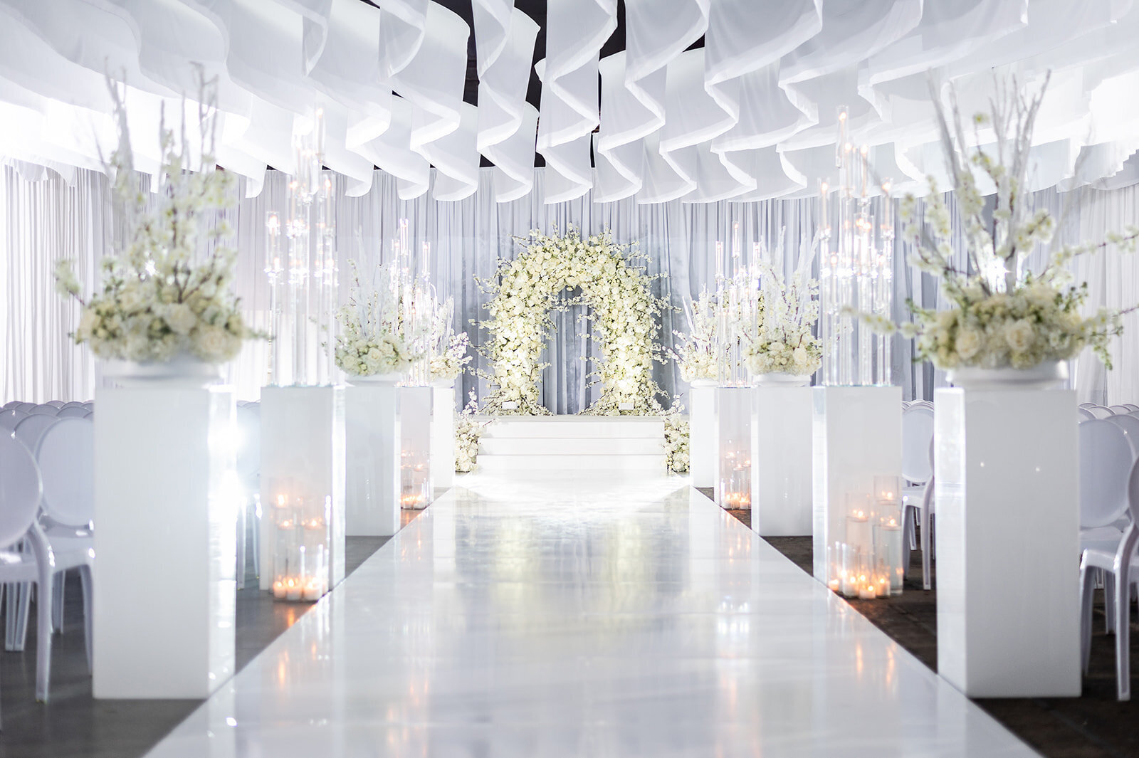 Elegant all-white wedding ceremony at The Kent in downtown Memphis, TN featuring modern floral arch, luxury white aisle, ambient candlelight, and event design by Wells Design Co.