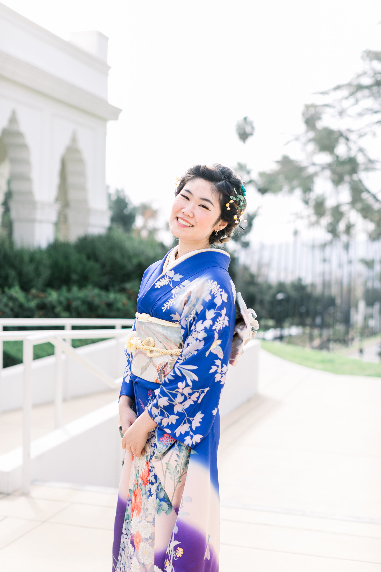 Cheerful young woman in a blue furisode kimono posing outside the historic Brand Park Glendale for her coming-of-age ceremony. Perfect for kimono rental in Los Angeles | ブランドパーク（グレンデール）の屋外で成人式を祝う青い振袖姿の女性、ロサンゼルスで着物レンタル