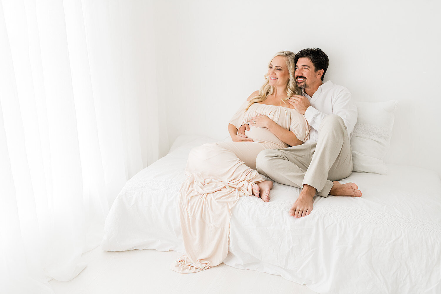a pregnant couple waiting on their baby while sitting on a white bed