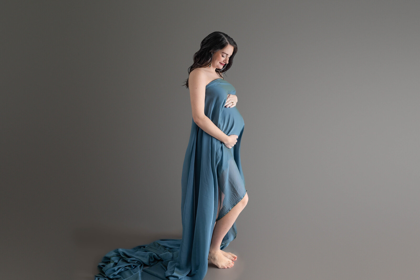 A pregnant woman draped in a blue fabric and posing for her maternity pictures in Huntsville Alabama