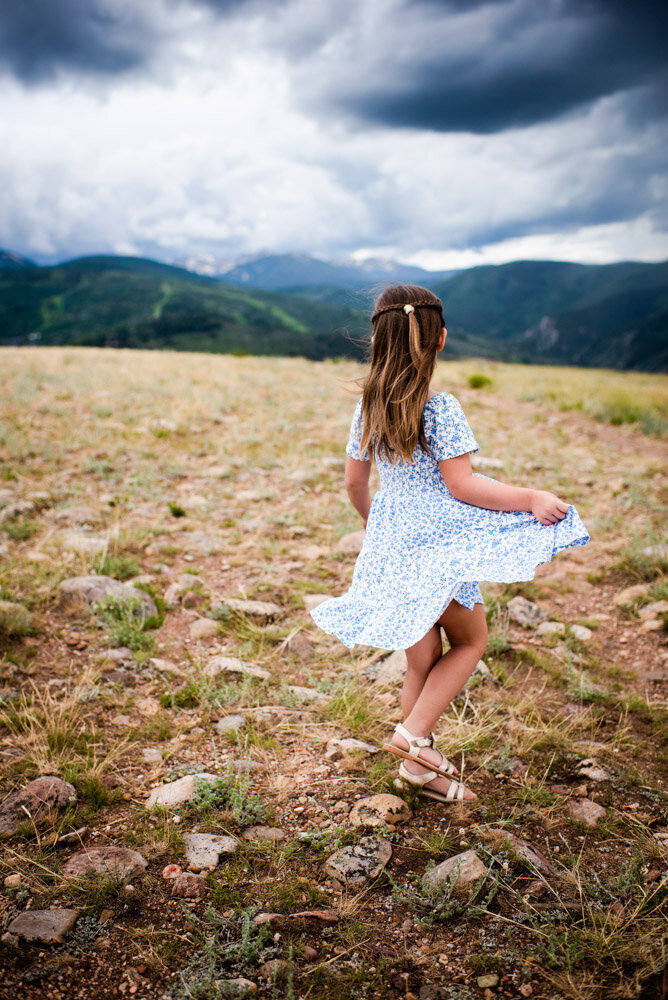 a little girl twirls around in her blue dress on a mountain top in Colorado