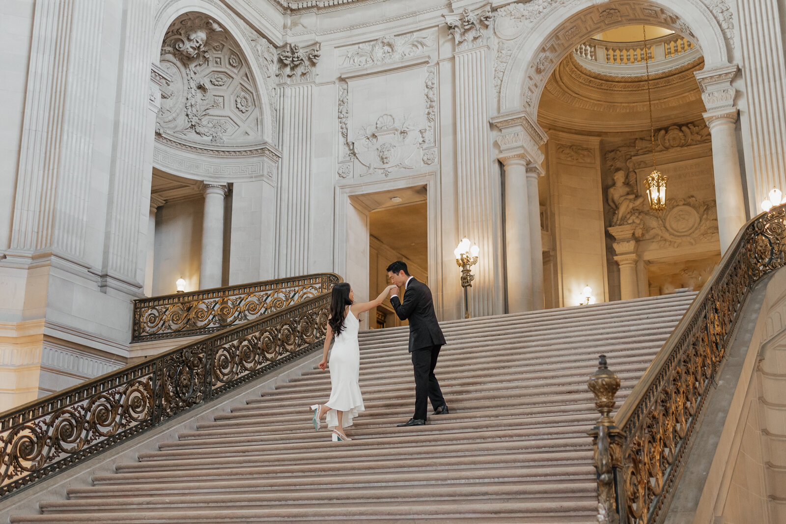                                      couple walking up the steps of san francisco city hall while he kisses her hand