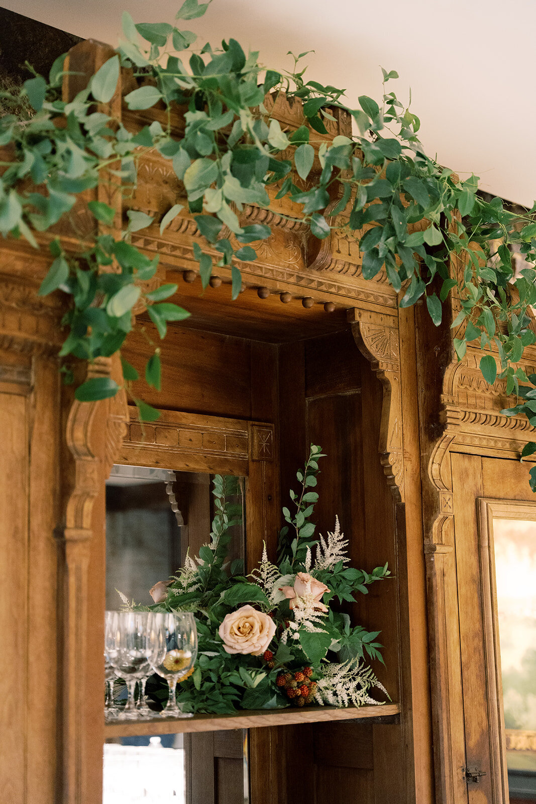 Antique wooden shelf with floral arrangement tucked in it and smilax greenery vining along the molding.