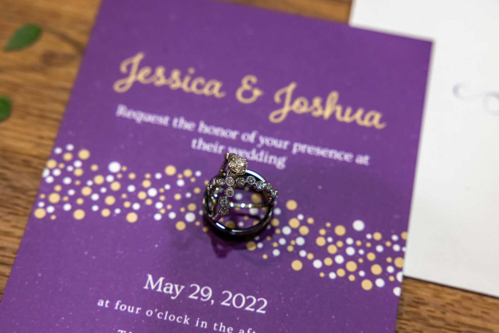 A pair of wedding rings displayed on a purple wedding invitation featuring gold details, captured at a Chetola Resort wedding in Blowing Rock, NC, showcasing personalized and elegant wedding day elements.