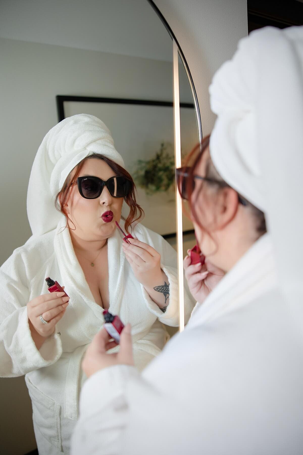 Confident woman in a white robe and towel wrap applies red lipstick in front of a mirror during a personal branding photoshoot in Seattle. Captured by a Seattle brand photographer, this image from the “She Plays With Fire” session highlights luxury, empowerment, and self-expression for women entrepreneurs.