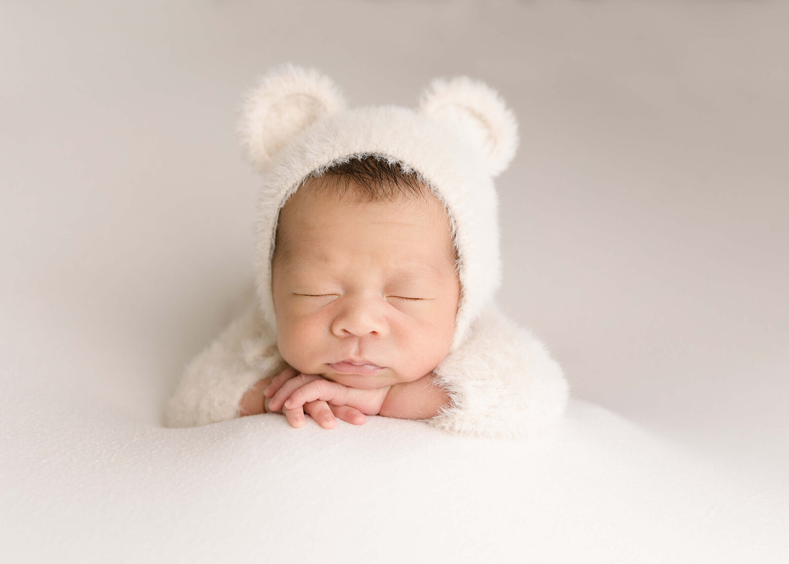 Baby boy in teddy bear fuzzy out posed with chin on hands by Ashley Nicole Photography.