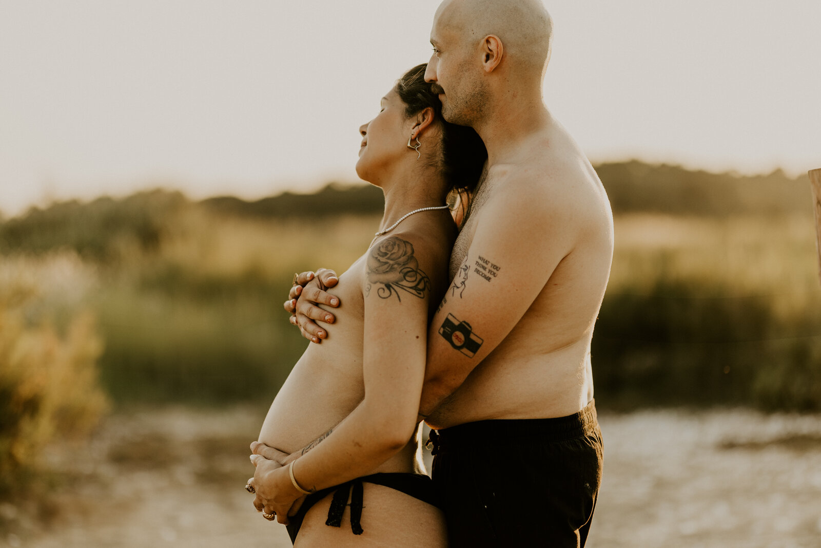Couple en bord de mer, la femme enceinte en robe beige tient son ventre et pose tendrement contre son partenaire. Capturée par Laura, photographe en vendée.