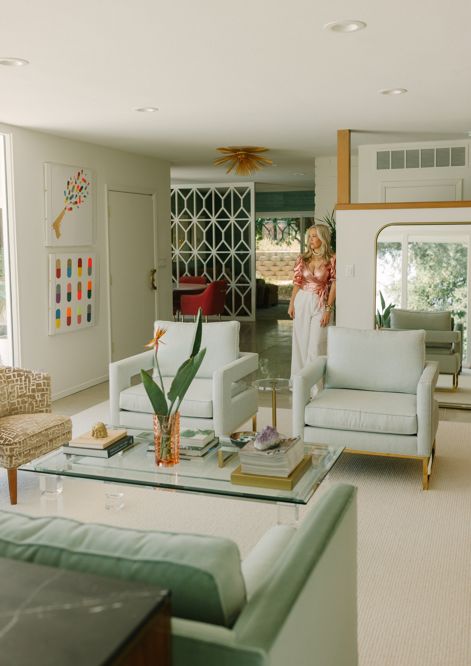 Editorial branding portrait of a stylish woman standing in a luxe midcentury modern living room with soft natural light and colorful interior design details.